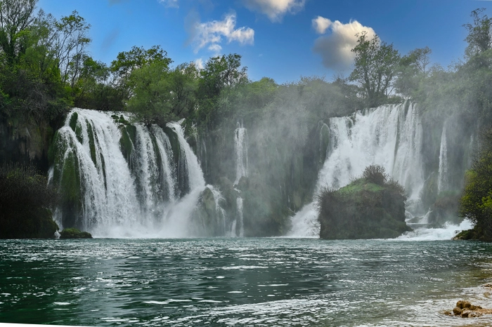Das Rauschen wilden Wassers, üppige Grün- und Blautöne, Sonnenlicht, das in der aufgewirbelten Gischt funkelnd bricht: Unweit von Mostar liegt mit den 120 Meter breiten Kravica Wasserfällen eines der schönsten Naturspektakel Bosniens. Längst kein Geheimtipp mehr, sind die Fälle hier dennoch weit weniger stark besucht als jene der Plitvicer Seen und der Krka Wasserfälle im benachbarten Kroatien. Und so ist das Schwimmen im glasklaren Wasser hier noch erlaubt.