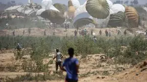 Palestinians rush to the site where parachuted aid packages are landing in the Nuseirat area in the central Gaza Strip during an airdrop above the Israel-besieged Palestinian territory on August 6, 2025. (Photo by Eyad BABA / AFP)