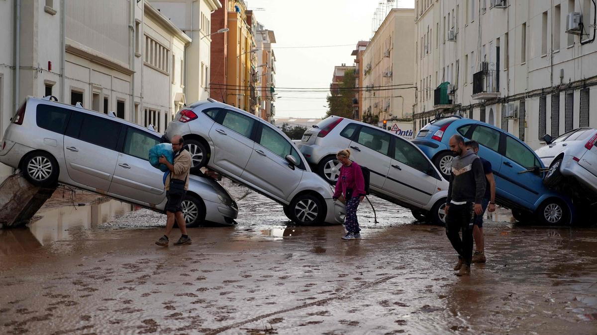 Residents walk past piled up cars following deadly floods in Sedavi, south of Valencia, eastern Spain, on October 30, 2024. Floods triggered by torrential rains in Spain's eastern Valencia region has left at least 70 people dead, rescue services said on October 30. (Photo by Manaure QUINTERO / AFP)