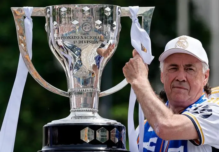 Real Madrid's Italian coach Carlo Ancelotti holds the 36th Spanish La Liga trophy of his team as Real Madrid players parade onboard a bus to celebrate at the Cibeles square in Madrid on May 12, 2024. Real Madrid's fans line the streets of Madrid as 'Los Blancos' celebrate their 36th Liga trophy before facing Borussia Dortmund at Wembley in the Champions League football final on June 1. (Photo by OSCAR DEL POZO / AFP)