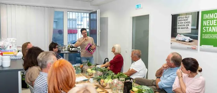Eine Gruppe von Menschen sitzt an einem langen Tisch voll mit Gemüse und Zubehör zum Fermentieren