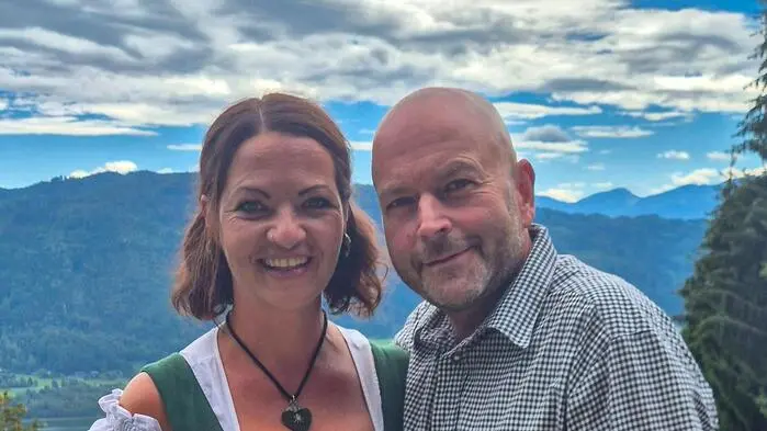 Eine Frau und ein Mann in Tracht stehen auf einer Terrasse mit weitläufigem Blick ins Tal