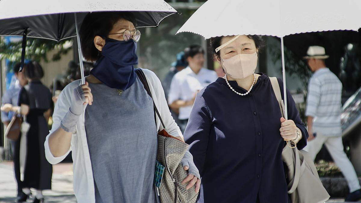Die Menschen schützen sich mit Schirmen und Masken vor der Hitze