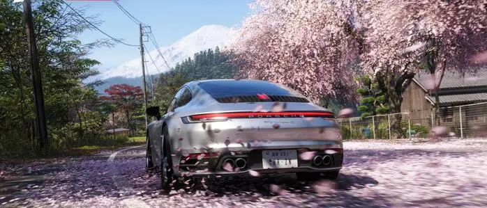 Ein Porsche fährt auf einer Straße, die mit rosa Kirschblüten bedeckt ist. In der Ferne sieht man den Berg Fuji