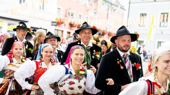 Mehrere Menschen in Tracht haben sich in Formation aufgestellt und lächeln in die Kamera