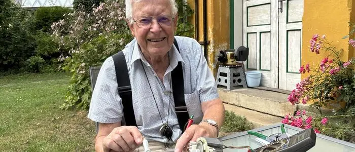 Ein älterer Mann mit Brille sitzt an einem Tisch und bedient ein elektrisches Gerät