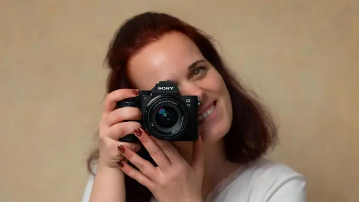 Eine Frau in weißem Shirt hält eine Kamera vor das Gesicht