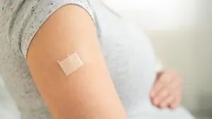 Close-up of expecting mother with bandage on forearm post-immunization. Thoughtful moment of prenatal healthcare and maternal protection.