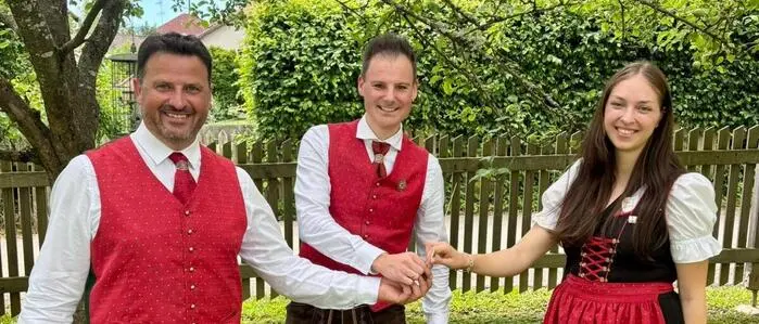 Zwei Männer und eine Frau, alle in Tracht, lächeln in die Kamera.