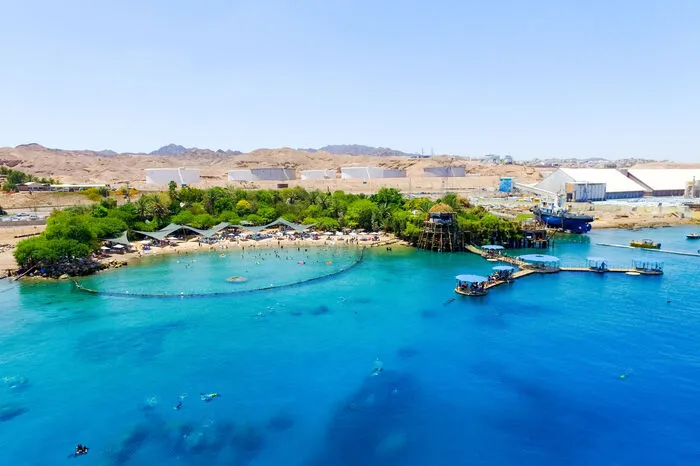 Dolphin-Reef-Beach, Israel. Der Dolphin Reef Beach liegt an der südlichen Spitze Israels am Roten Meer in unmittelbarer Nähe der Touristenstadt Eilat. Die hier knapp 12 km lange Küstenlinie ist Israels einziger Zugang zum Indischen Ozean. An diesem Strand erwartet Besucher ein ganz besonderer Ort: Die Anlage des Dolphin Reef ist das weltgrößte Meeresgehege und beherbergt fünf Delfine, drei Weibchen und zwei Männchen. Diese können das Gehege verlassen können, wann immer sie wollen. Durch ein Tor können die Tiere in das offene Meer schwimmen, aber auch wieder zurückkommen. Die Einrichtung legt hohen Wert darauf, dass der freie Wille der Delfine gewahrt wird.