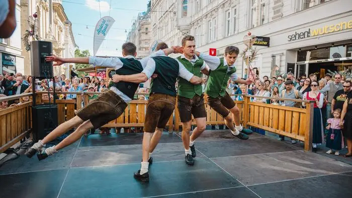 Vier Schuhplattler tanzen auf einem Tanzboden in der Grazer Herrengasse