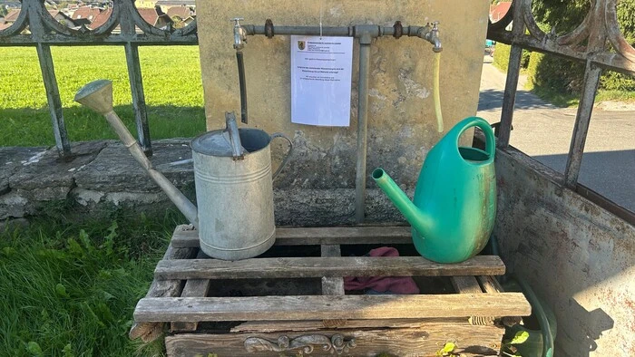 Zwei Gießkannen stehen bei einem Brunnen