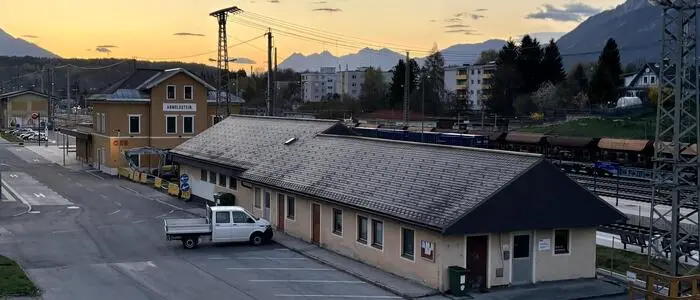 Seitliche Vogelperspektive eines flachen Gebäudes neben einem Gleis, davor steht ein Lieferwagen