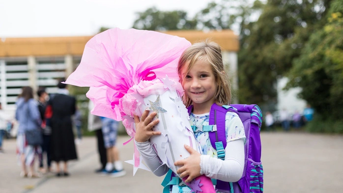 Ein Mädchen mit violetter Schültasche hält eine pinke Schultüte in Händen