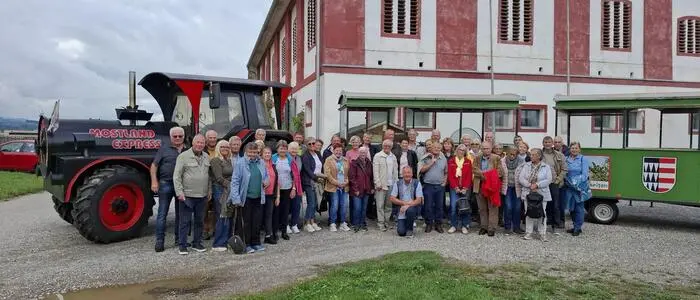 Eine große Gruppe Senioren steht neben einem Traktor auf einem Bauernhof
