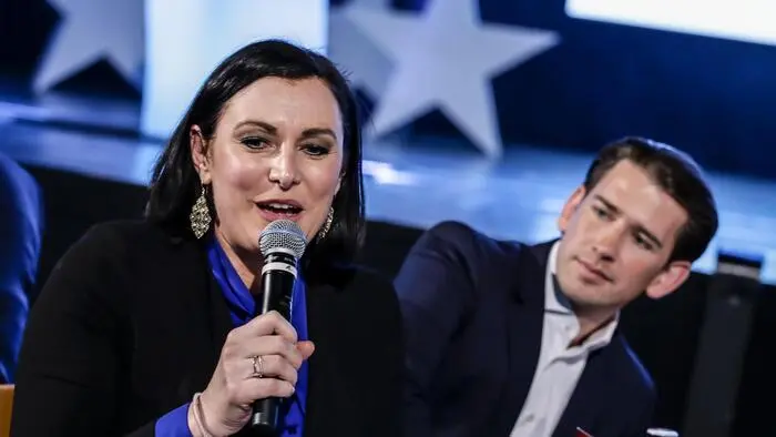 Elisabeth Köstinger spricht in ein Mikrofon, Sebastian Kurz schaut ihr von hinten über die Schulter.