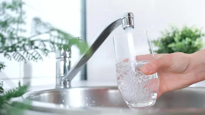 Ein Glas Wasser, das bei einem Wasserhahn aufgefüllt wird