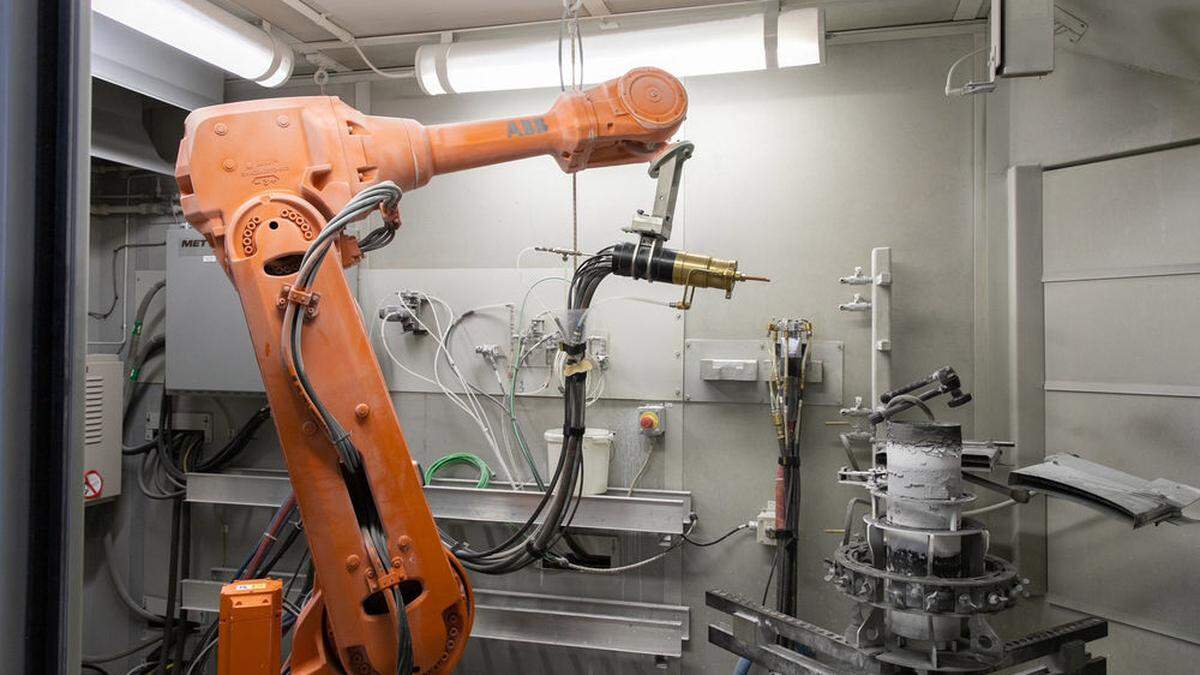 Mithilfe eines Roboterarms werden Wärmedämmschichten auf Testobjekte gespritzt.