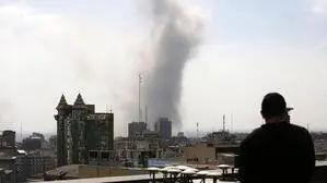 Eine Rauchsäule steigt in Teheran auf. Im Vordergrund ist ein Mann von hinten zu sehen, der Richtung Rauchsäule blickt.