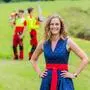 Eine Dame im Dirndl, hinter ihr sieht man zwei Waldarbeiter.