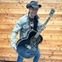 Mann mit Jeansjacke, Cowboyhut und schwarzer Gitarre | Seltene Gitarren wie diese halbakustische Elvis-Presley-Gibson und andere Originale zeigt der Elvis-Missionar genauso wie zahlreiche Devotionalien und Filmmaterial