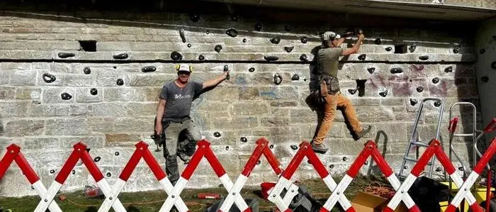 Zwei Männer montieren Klettergriffe an einer Wand, davor steht eine Absperrung
