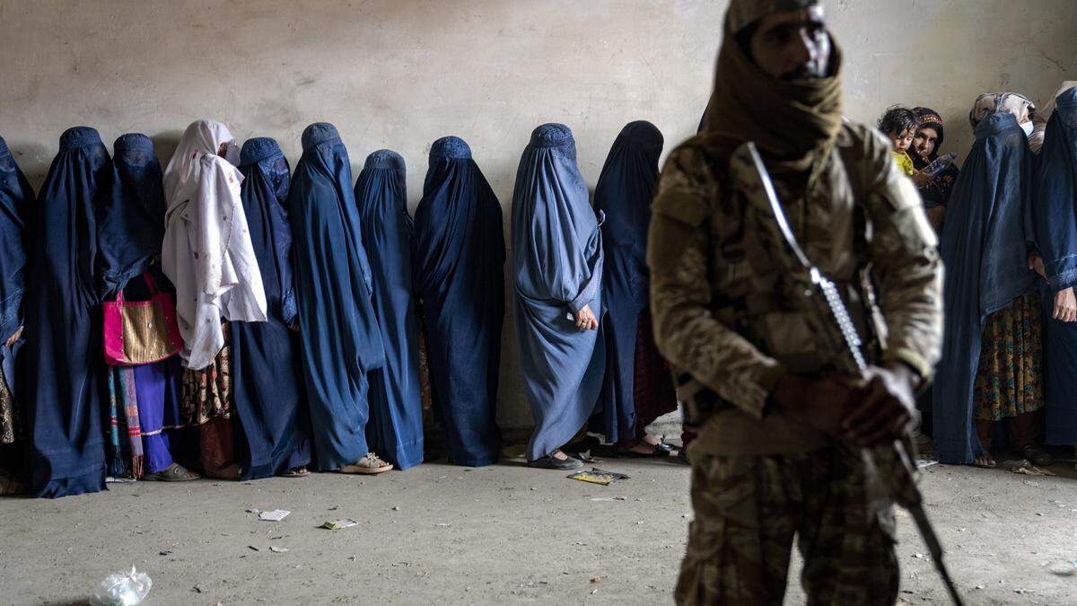 Ein Taliban-Krieger überwacht verschleierte Frauen, die sich für Essensrationen anstellen 