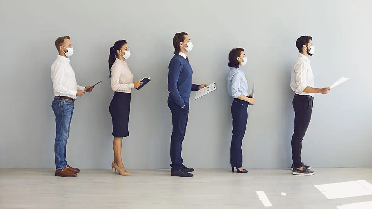 Job seekers wearing face masks standing in row keeping safe distance while waiting for job interview