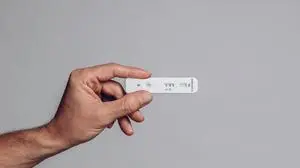 hand holds covid antigen test showing positive result on gray background in study shot