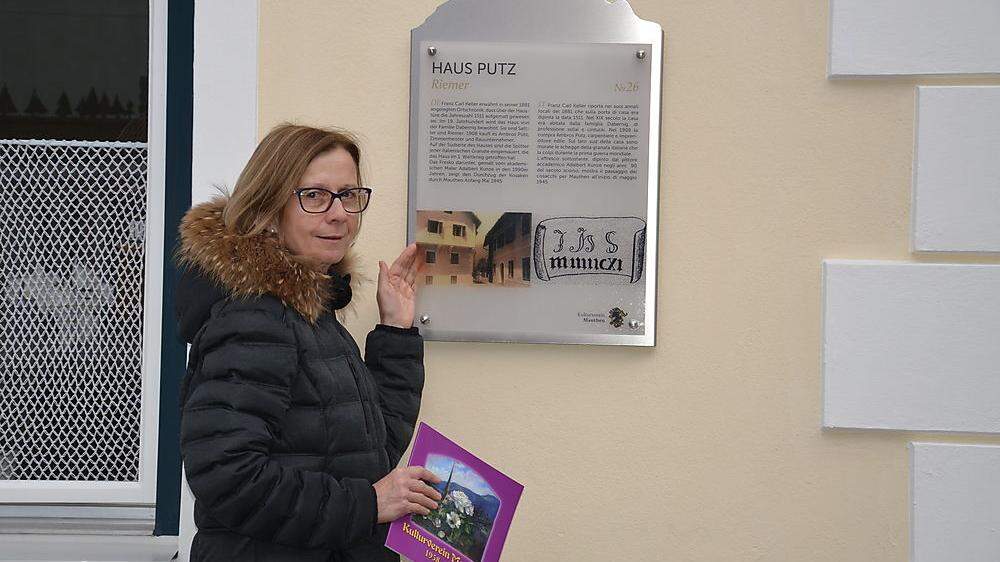 Ilse Durchner vor dem Haus Putz und dessen Haustafel über die Geschichte des Ortes