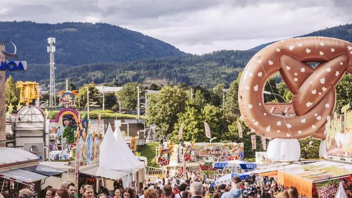Blick auf ein Festgelände mit Fahrgeschäften, Standln und vielen Gästen