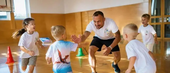 Ein Mann, Anfang 40, trainiert Kinder in einer Turnhalle.