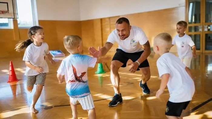 Ein Mann, Anfang 40, trainiert Kinder in einer Turnhalle.
