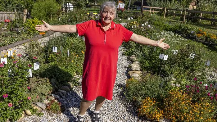 Eine Dame im roten Kleid streckt inmitten eines Kräutergartens ihre Hände aus