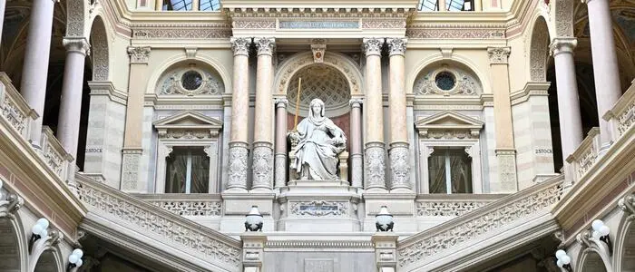 Das Bild zeigt die Eingangshalle des Justizpalasts in Wien, wo der oberste Gerichtshof sitzt. Eine breite Treppe führt aus der Eingangshalle in die oberen Stockwerke