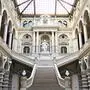 Das Bild zeigt die Eingangshalle des Justizpalasts in Wien, wo der oberste Gerichtshof sitzt. Eine breite Treppe führt aus der Eingangshalle in die oberen Stockwerke