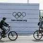 Cyclists pass in front of a banner calling for the Israeli team to be banned from the Paris 2024 Olympic Games, installed by the pro-Palestinian protesters in Jakarta on July 21, 2024. (Photo by Yasuyoshi CHIBA / AFP)
