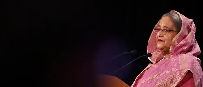 Bangladeschs Ex-Regierungschefin Sheikh Hasina spricht auf einem Rednerpult. Sie trägt ein rosafarbenes traditionelles Outfit. | Sheikh Hasina spricht von einem „politisch motivierten Urteil“