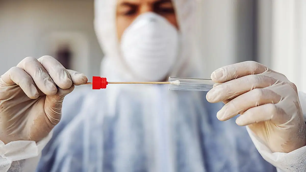 Man in protective suit with mask holding sample buccal cotton swab and test tube ready to collect DNA from the cells. Coronavirus covid-19. Infection prevention and control of epidemic. World pandemic.  World pandemic 