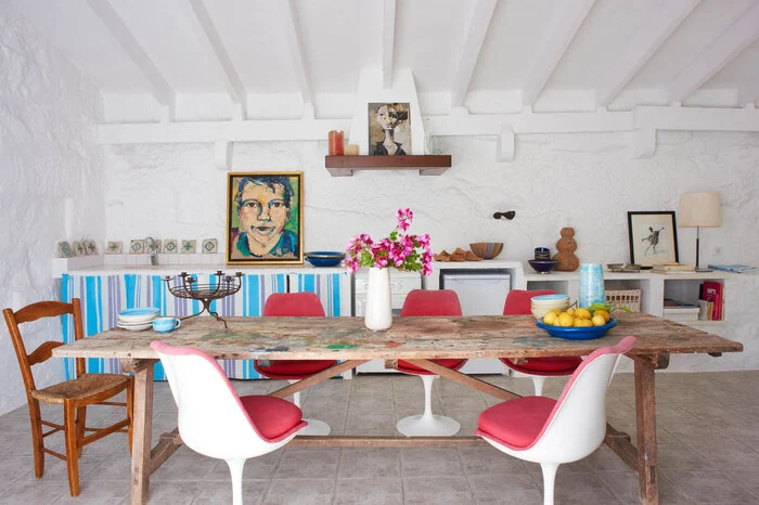 Exotisch originell - wie bei der spanischen Schuhdesignerin  Ursula Mascari auf Menorca: Künstlerische Porträts, handgetöpferte Keramik, Natursteinboden, ein umgenutzter Ateliertisch voller Farbkleckse und die Tulp-Stühle von Eero Saarinen ergänzen sich perfekt. Das Esszimmer ist ein gutes Bespiel für lockeres Kombinieren.