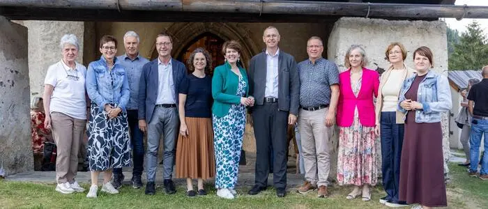Sieben Frauen und vier Männer stehen vor einer Kirche und lachen in die Kamera