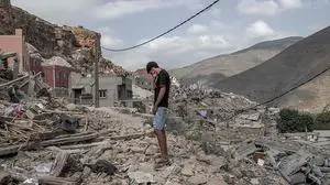 Ein junger Mann steht auf den Trümmern eines Hauses.