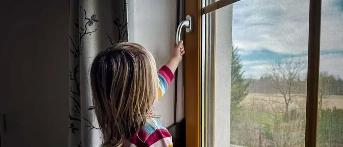 Mädchen in bunt gestreiftem Pullover greift zu einem Fenstergriff.