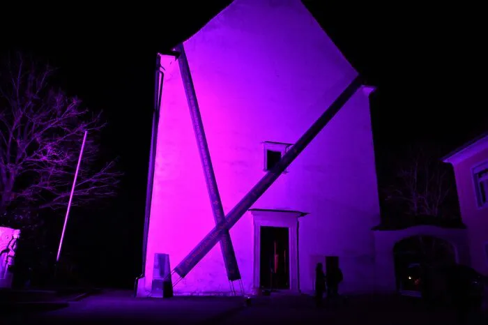 Bei Dunkelheit wird die Außenfassade der Florianikirche in Straden violett beleuchtet.