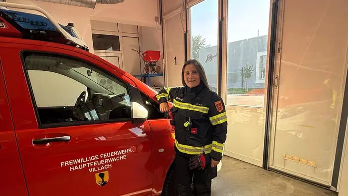 Eine junge Frau in Feuerwehruniform lehnt sich an ein rotes Feuerwehrauto an in einer Halle