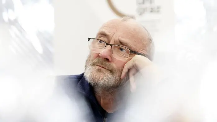 Phil Collins lehnt sich auf seine Hand und blickt nach oben.