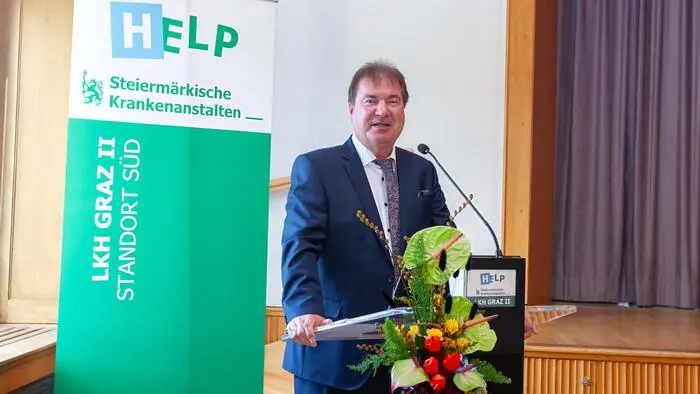 Ein Mann im dunkelblauen Anzug steht vor einem Stehpult und spricht gerade in ein Mikrofon.