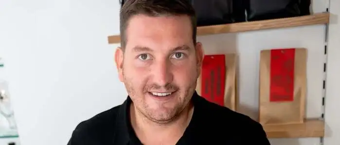 Ein Mann mit schwarzem Hemd schneidet eine Torte auf 