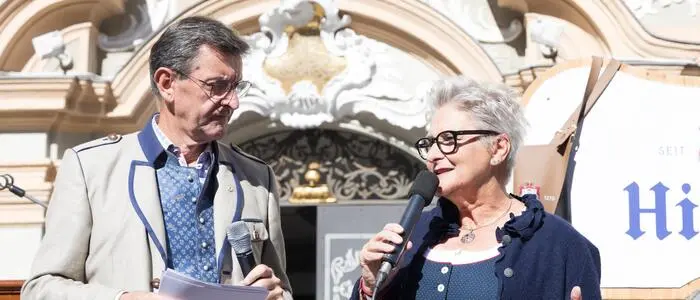 Eine Frau und ein Mann stehen auf einer Bühne. Die Frau spricht ins Mikrofon.
