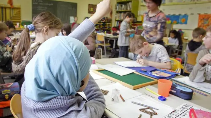 Das Bild zeigt ein Mädchen mit einem Kopftuch in einem Klassenzimmer